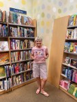 Author Lisa Galdos smiling in a bookstore children’s section, holding her BIG HUGS for Kids book while standing between shelves of picture books.